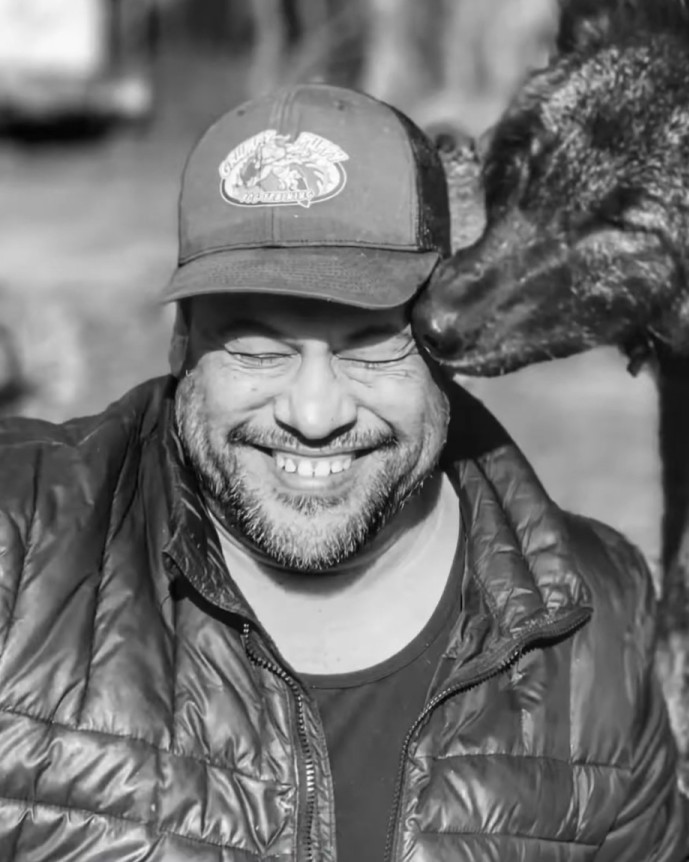 Tony Nila smiling as a wolfdog affectionately nuzzles his cap